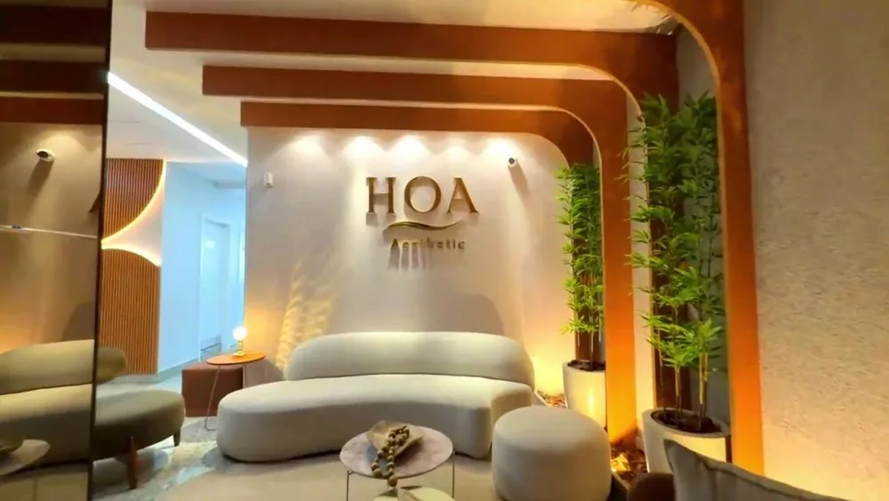 Sala de espera e recepção da HOA Aesthetic, com sofá curvo e o letreiro dourado da marca